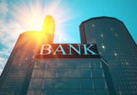 A tall glass building with "Bank" written on the front and a sunbeam behind the building